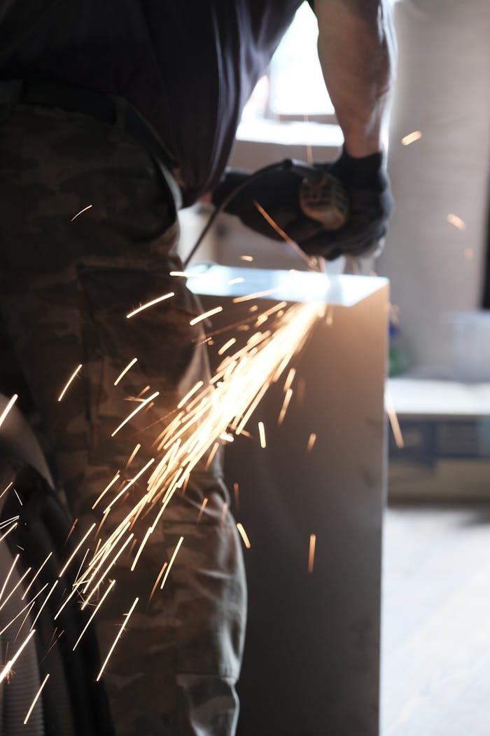 A person grinding metal indoors creating bright sparks in an industrial setting.